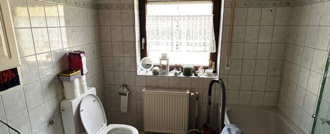 Ein altes Badezimmer vor der Renovierung mit Toilette, badewanne und einem in die Jahre gekommenen Waschtisch.