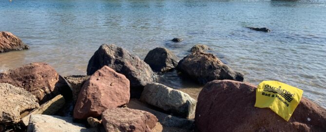 Ein Handtuch das mit dem Günther-Logo versehen ist, liegt am meer auf einem stein