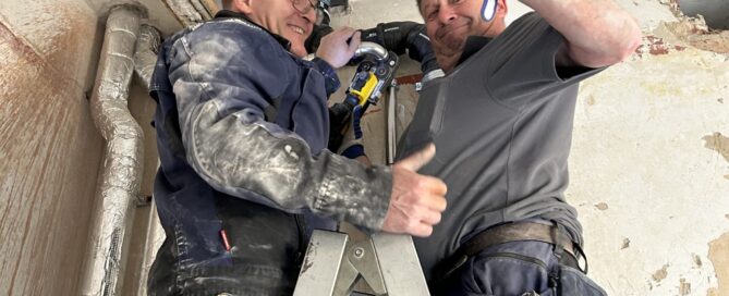 Zwei Mitarbeiter der Firma Günther aus Mannheim sind auf eine Leiter gestiegen und zeigen ihre Muskeln zur Demonstartion von Stärke.